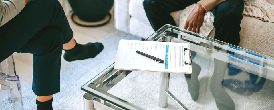 Two people sit on a sofa with a clipboard and pen on a glass table between them. Two people sit on a sofa with a clipboard and pen on a glass table between them.